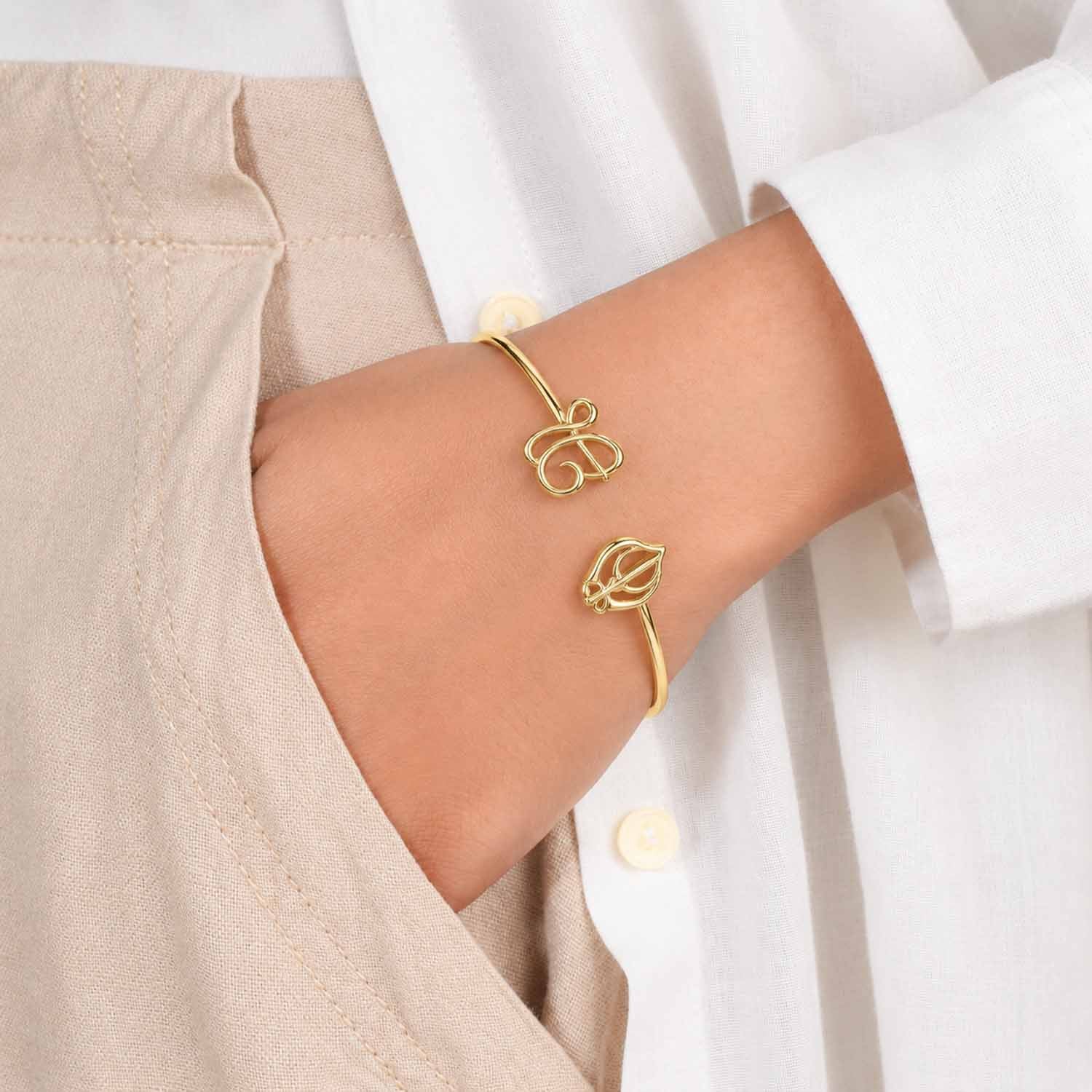 Gold open cuff bangle with Ik Onkar and Khanda motifs, worn on the wrist with a neutral outfit.