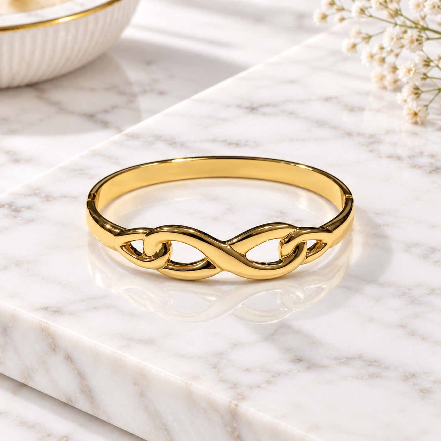 Polished gold-tone infinity design bangle displayed on a marble surface.