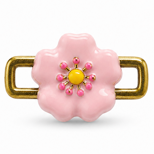Pink flower-shaped jewellery charm featuring a glossy pastel pink enamel-style flower with scalloped petals, a yellow round center, and small pink and gold bead-like accents arranged in a floral pattern. The charm is attached to a polished gold-tone rectangular open-link frame on both sides, creating a playful, feminine design.