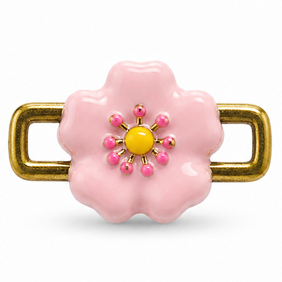 Pink flower-shaped jewellery charm featuring a glossy pastel pink enamel-style flower with scalloped petals, a yellow round center, and small pink and gold bead-like accents arranged in a floral pattern. The charm is attached to a polished gold-tone rectangular open-link frame on both sides, creating a playful, feminine design.
