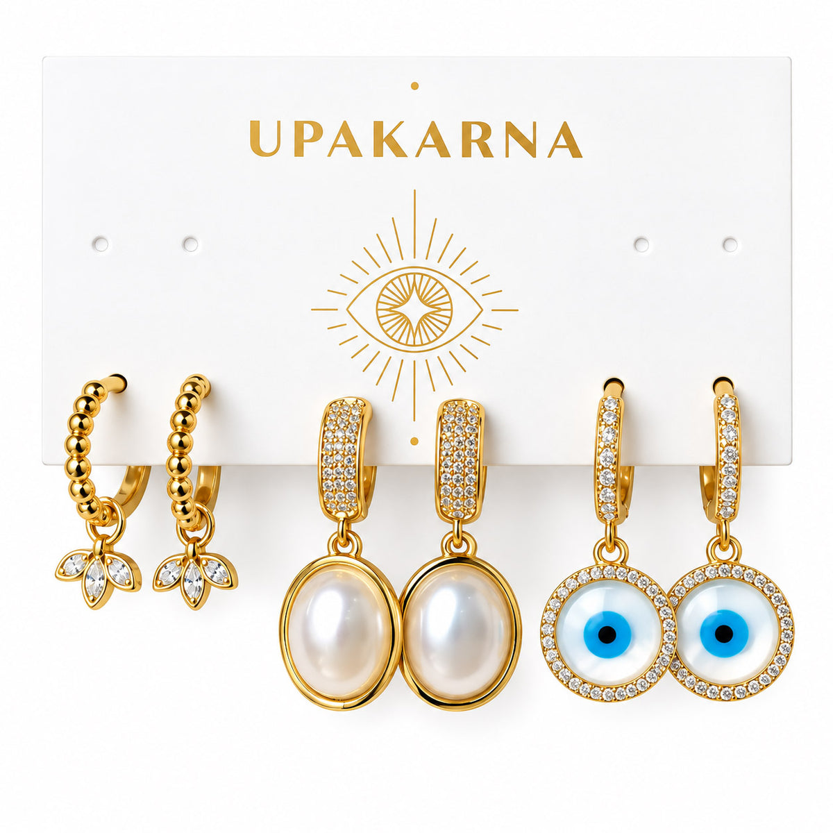 Upakarna earring display card featuring three pairs of gold earrings: beaded floral hoops, pearl drop earrings, and crystal evil eye drop earrings on a clean white background.