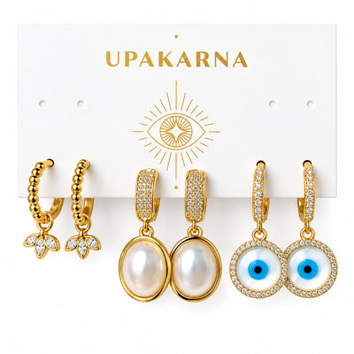 Upakarna earring display card featuring three pairs of gold earrings: beaded floral hoops, pearl drop earrings, and crystal evil eye drop earrings on a clean white background.