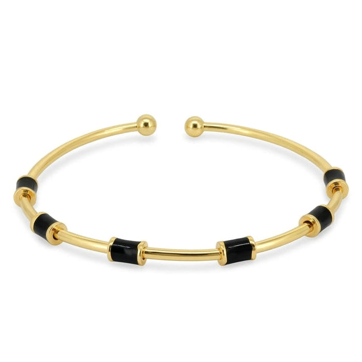 Anti-tarnish yellow gold open cuff bracelet featuring a slender polished band set with cylindrical black enamel station tubes and smooth spherical ball terminals, on a solid white background.