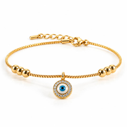 Gold-tone anklet featuring a round blue evil eye pendant surrounded by sparkling clear stones, with polished gold bead accents and a delicate box chain. Adjustable extension chain and lobster clasp, displayed on a pure white background.