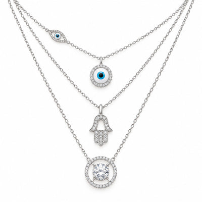 Upakarna silver layered necklace set featuring an evil eye chain, crystal evil eye pendant, Hamsa hand pendant, and solitaire circle pendant on a clean white background.