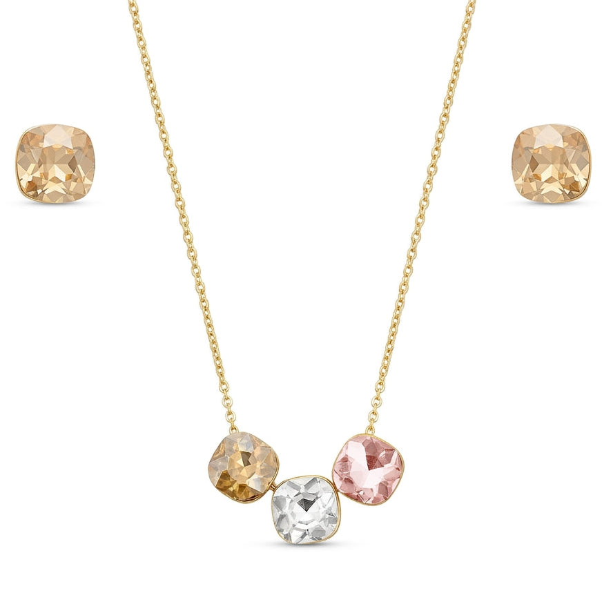 A gold jewelry set isolated on a plain white background, featuring a delicate fine-chain pendant necklace adorned with three cushion-cut faceted crystals in champagne, clear, and soft blush pink. The set is completed by a pair of matching square cushion-cut champagne crystal stud earrings.