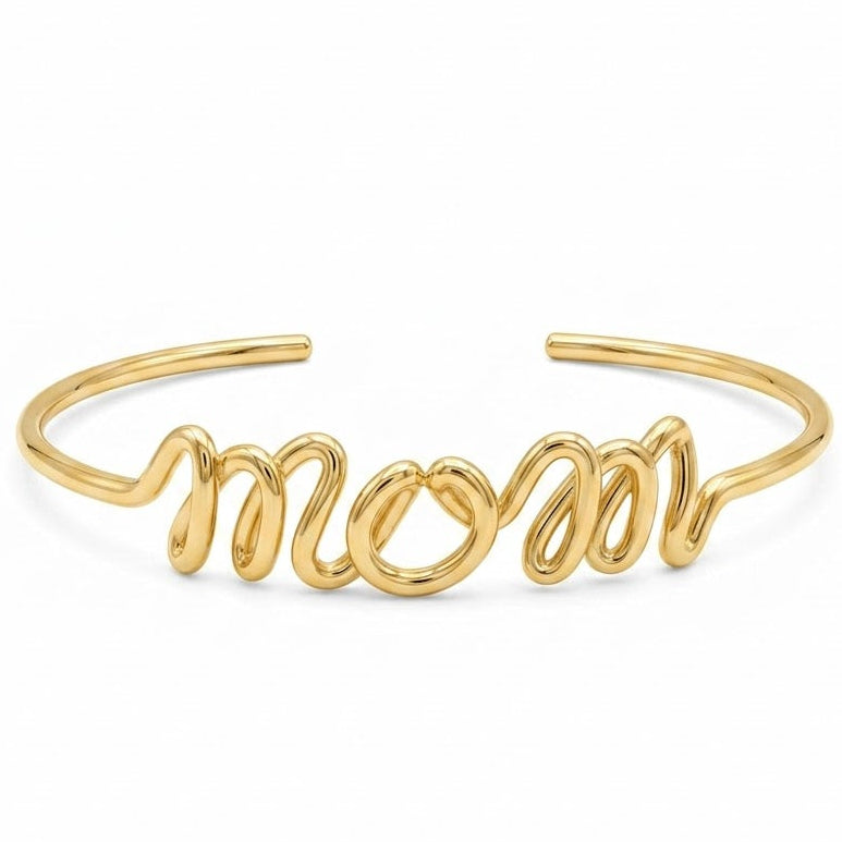Anti-tarnish yellow gold open cuff bracelet featuring a central, flowing cursive "mom" wire-script design on a smooth, rounded polished band.