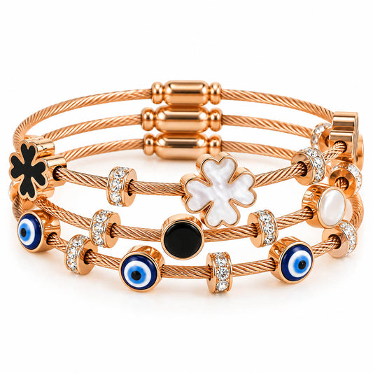 A studio shot of a curated stack of multi-strand rose gold cable wire bracelets, showcasing stations of blue evil eye beads, a white mother-of-pearl four-leaf clover, a black enamel clover, and sparkling rhinestone-paved ring spacers.