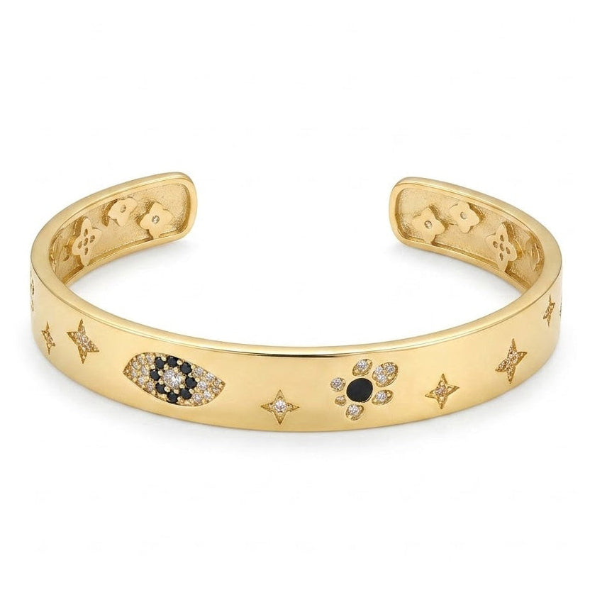 Anti-tarnish yellow gold wide open cuff bracelet featuring inlaid celestial starbursts, a pavé black and clear cubic zirconia evil eye, and a flower motif on a smooth flat band.