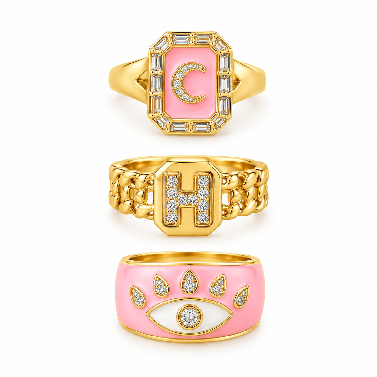 Three gold statement rings featuring a pink initial C signet ring, a chunky pavé H chain-link ring, and a bold pink evil eye enamel ring with crystal accents on a clean white background.