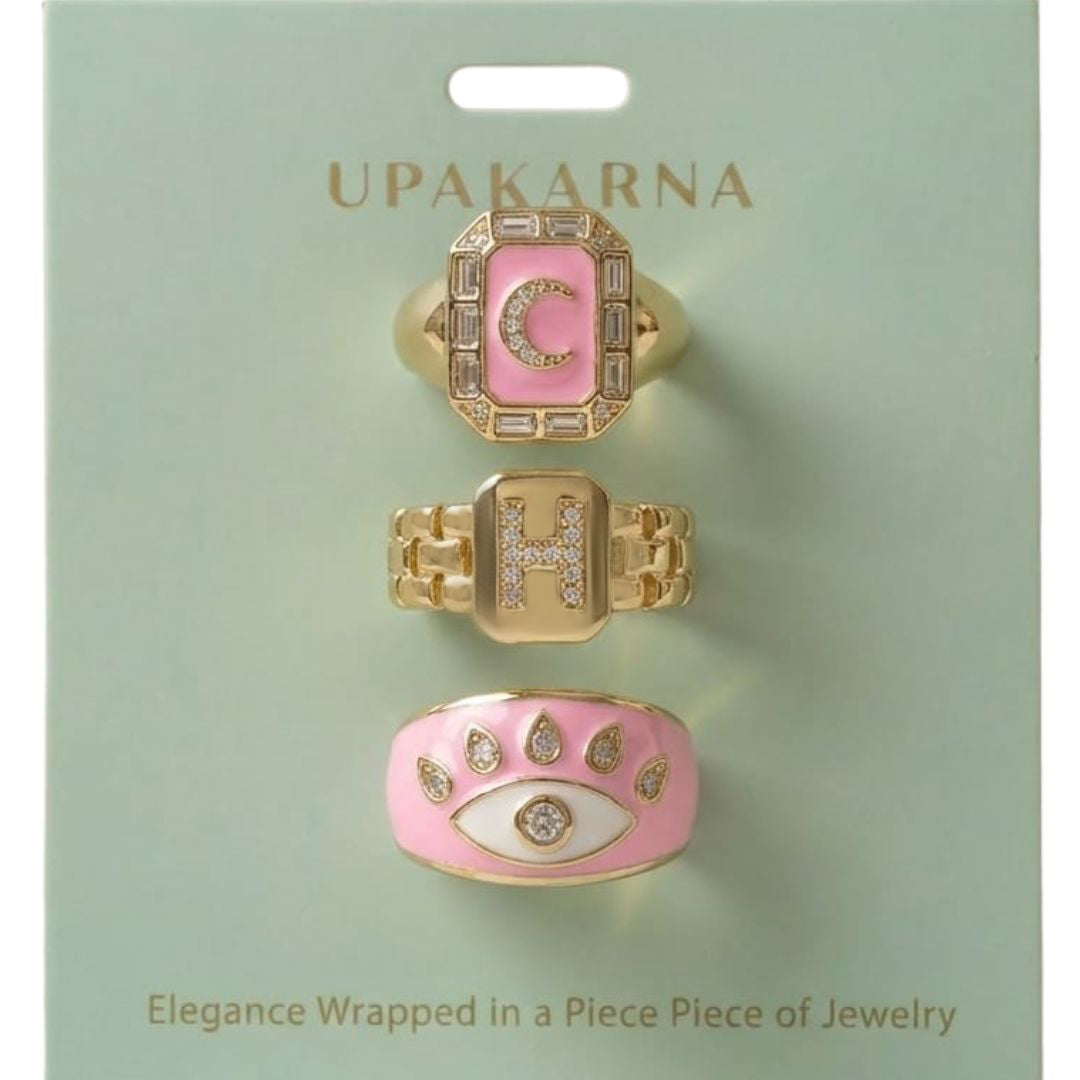 A stack of three adjustable gold rings featuring a pastel evil eye, a celestial moon motif, and a personalized initial charm.