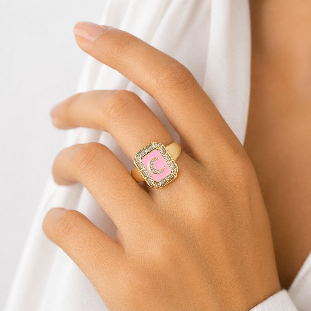 A stack of three adjustable gold rings featuring a pastel evil eye, a celestial moon motif, and a personalized initial charm.