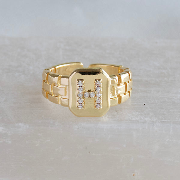 A stack of three adjustable gold rings featuring a pastel evil eye, a celestial moon motif, and a personalized initial charm.