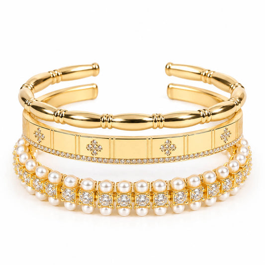 A product photo of a stacked set of gold-tone bracelets featuring segmented bamboo-style cuffs, a panel band with rhinestone clovers, and a double-row pearl and crystal bracelet.