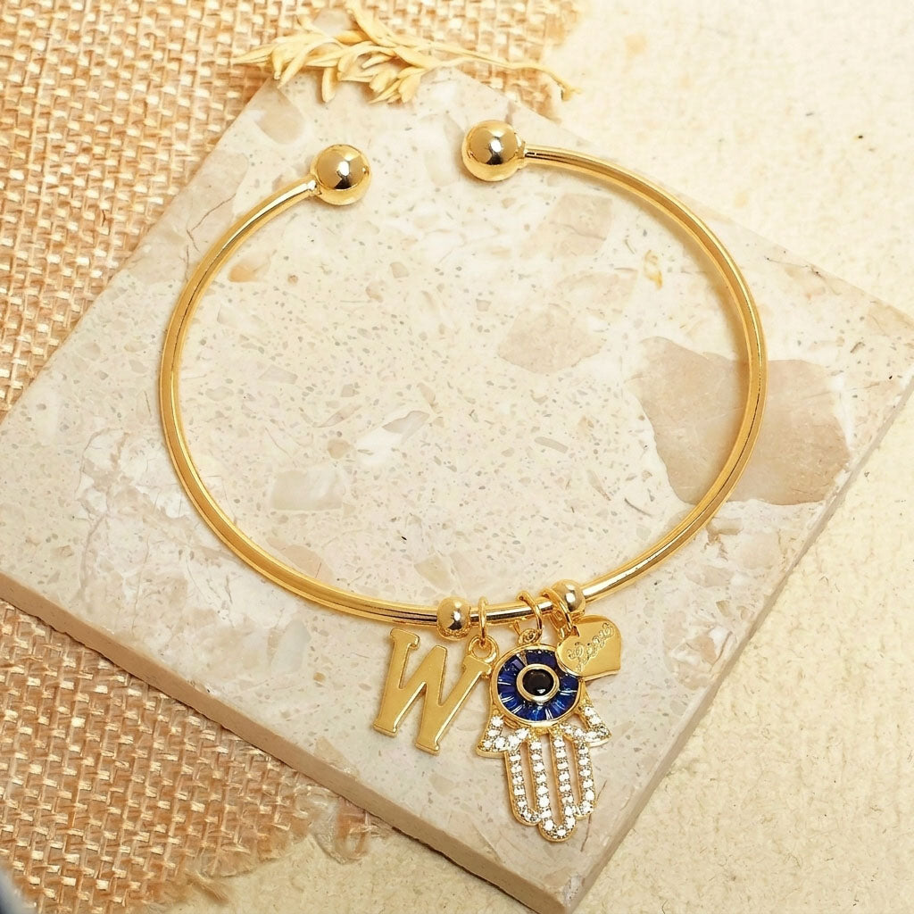 Elegant personalized Hamsa bracelet with an initial charm, heart charm, and evil eye detailing, crafted with an anti-tarnish finish for everyday wear, meaningful gifting, and lasting style.

