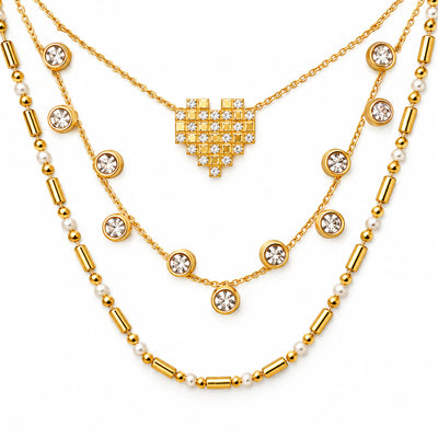 Upakarna gold layered necklace set featuring a crystal pixel heart pendant, bezel-set crystal station necklace, and pearl-bead chain on a clean white background.