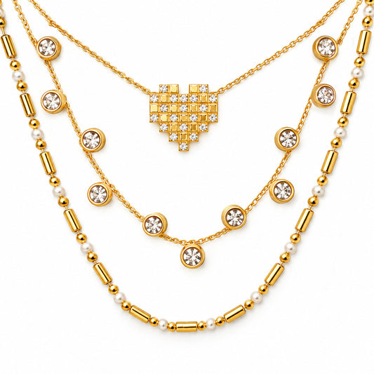 Upakarna gold layered necklace set featuring a crystal pixel heart pendant, bezel-set crystal station necklace, and pearl-bead chain on a clean white background.