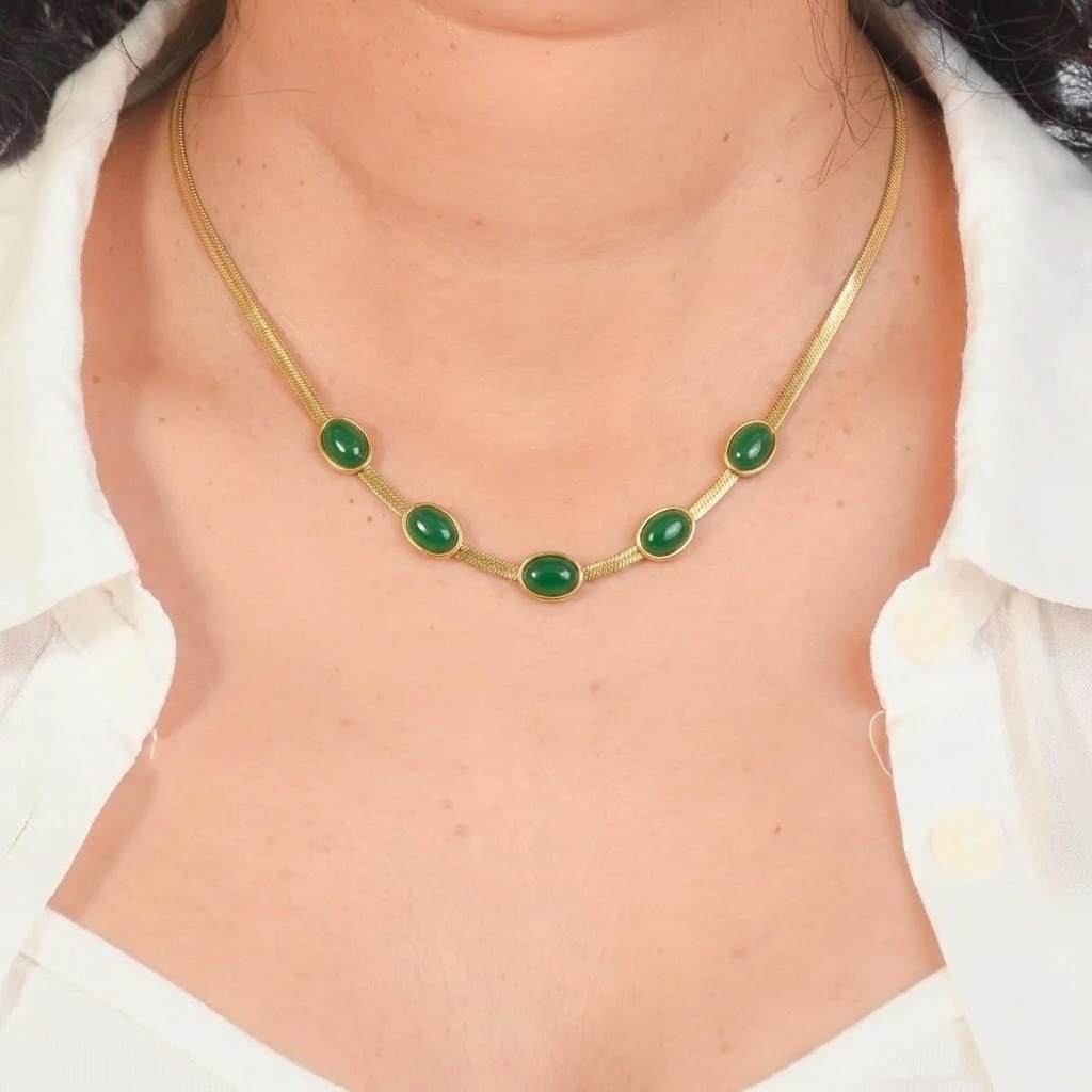 Close-up of a model wearing an elegant gold-tone snake chain necklace featuring five bezel-set oval green stones. The minimalist anti-tarnish necklace is styled with a white collared shirt, showcasing its refined design for everyday wear, office outfits, festive occasions, layering, and special events.