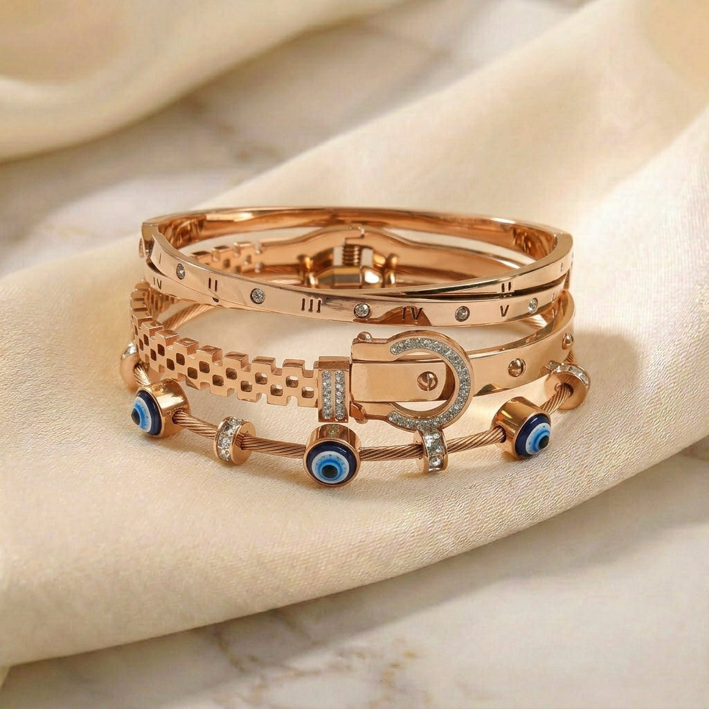 Luxury rose gold anti-tarnish bracelet stack featuring a Roman numeral bangle, crystal-studded buckle bracelet, textured chain bangle, and a blue evil eye cable bracelet, elegantly displayed on soft satin fabric.