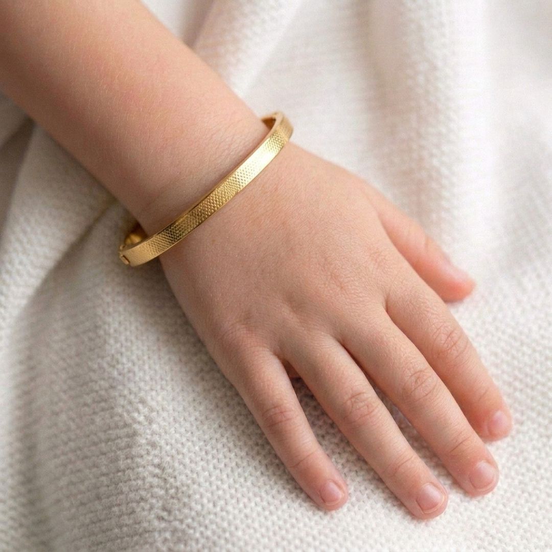 Minimalist gold stainless steel bangle bracelet with a slim textured band and secure hinged clasp, displayed on a clean white background.