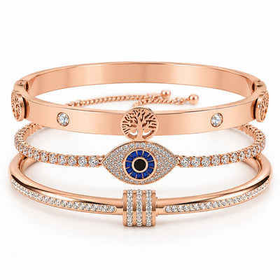 A product photo of a stacked set of rose gold bracelets featuring a hinge bangle with a Tree of Life pendant, a crystal tennis bracelet centered with a large evil eye charm, and a crystal-accented bangle with a paved barrel spacer.