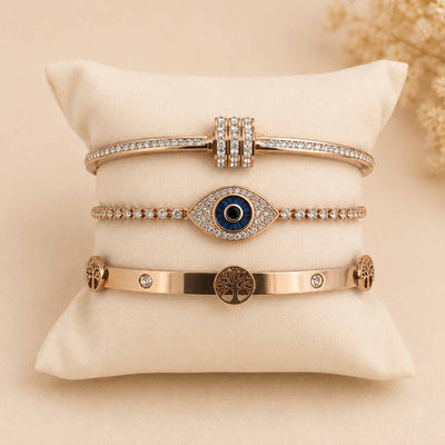 Rosegold bangle stack featuring a sparkling twisted bangle, Evil Eye tennis bracelet, and Tree of Life bangle displayed on a cream cushion.