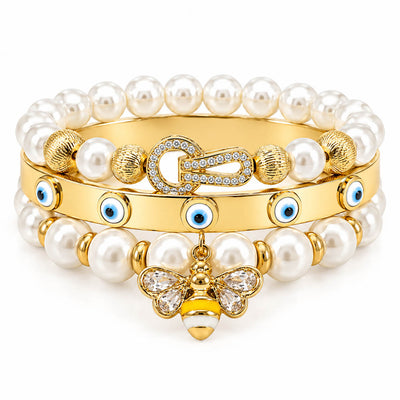A stack of three anti-tarnish gold-plated bangles featuring two pearl bead bangles with a crystal bee charm and textured gold beads, paired with a sleek evil eye bangle accented with blue enamel charms, creating a premium everyday jewellery stack on a clean white background.