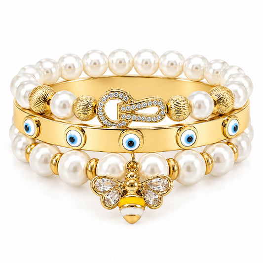 A stack of three anti-tarnish gold-plated bangles featuring two pearl bead bangles with a crystal bee charm and textured gold beads, paired with a sleek evil eye bangle accented with blue enamel charms, creating a premium everyday jewellery stack on a clean white background.