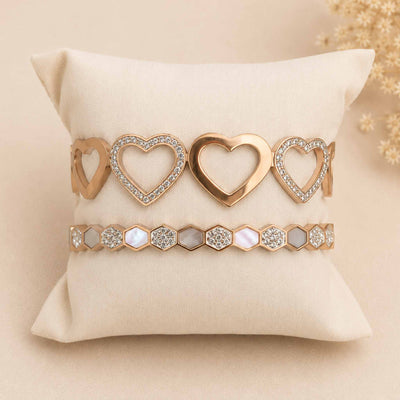 Golden anti-tarnish bangle stack featuring a studded multi-heart bangle and a patterned geometric bangle displayed on a cream cushion.