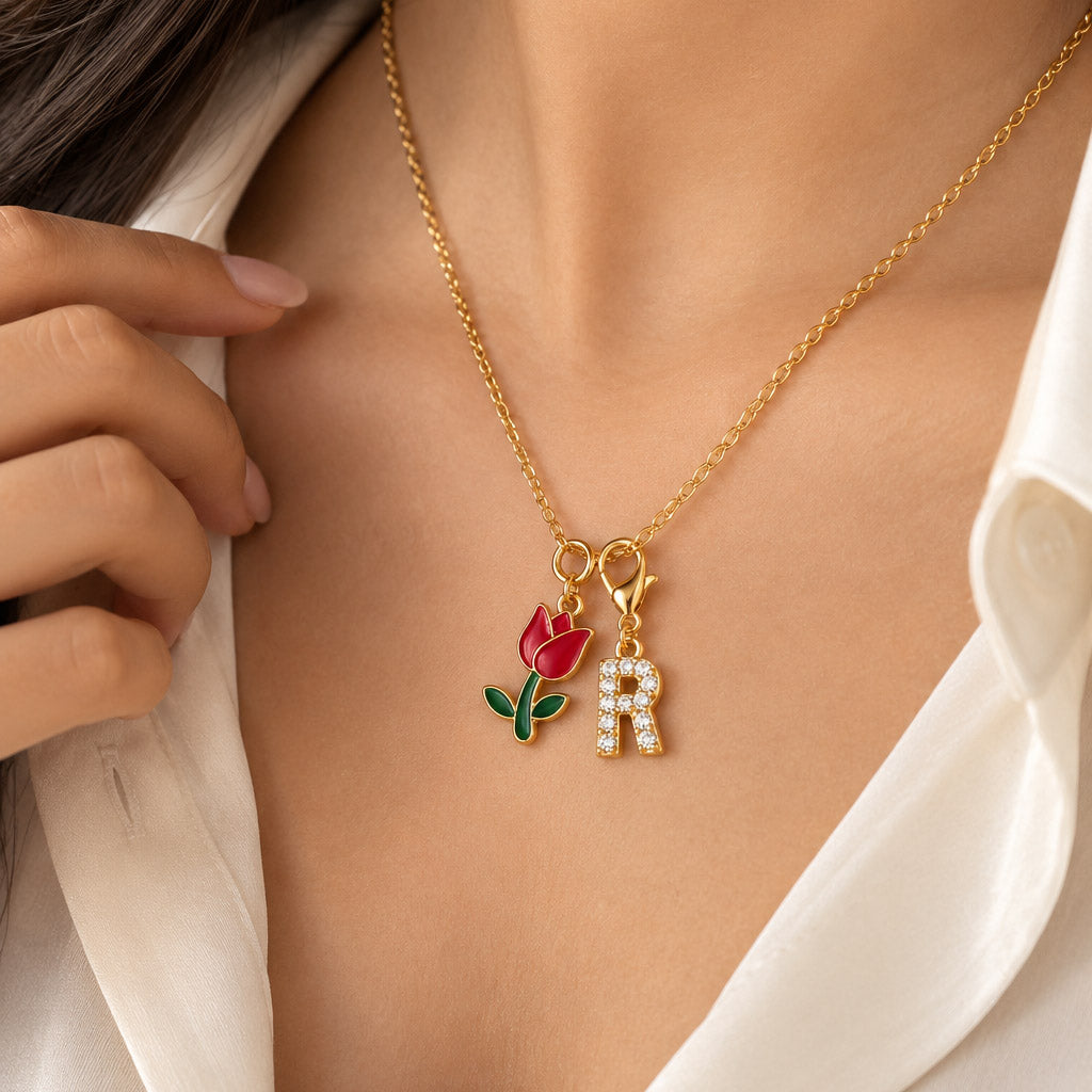 Gold-plated delicate chain necklace worn on a model, featuring a red tulip flower charm with green leaves and a sparkling “R” initial charm.