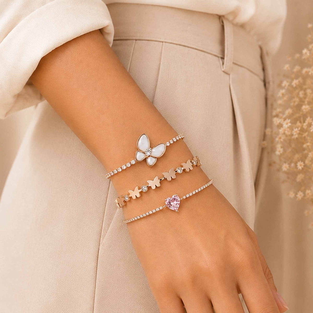 Rosegold butterfly bracelet stack worn on a woman’s wrist, featuring a mother of pearl butterfly bracelet, butterfly bangle, and pink heart bracelet.