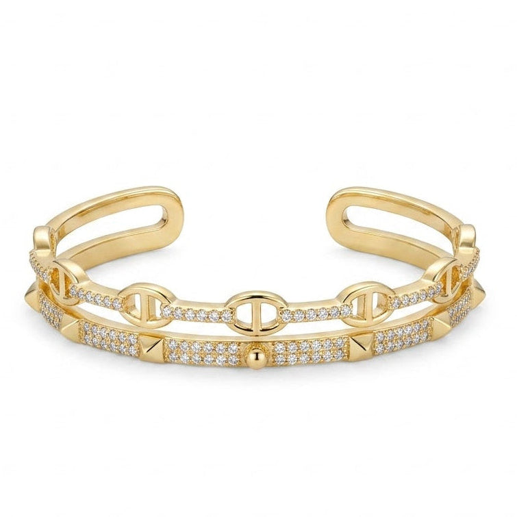 Anti-tarnish yellow gold open cuff bracelet featuring a layered double band with an upper mariner anchor link strand and a bottom pavé cubic zirconia strand accented with pyramid studs and a center sphere.