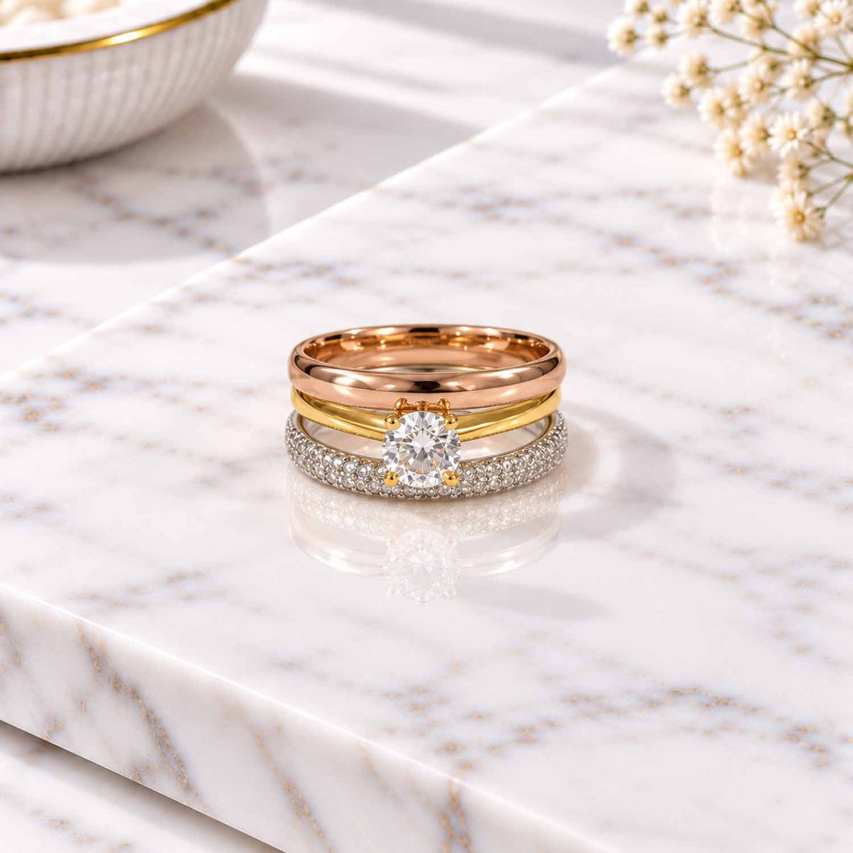 Rose gold, gold and silver three-ring stack with a sparkling round center stone on a marble surface.