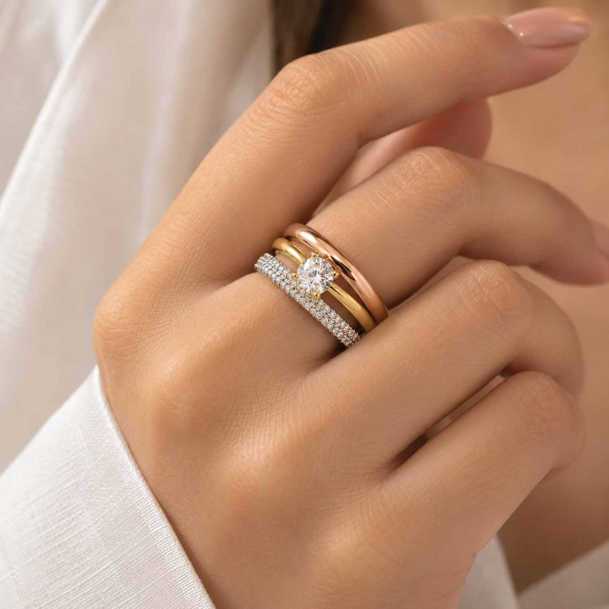 Close-up of a hand wearing a mixed-metal ring stack with rose gold, gold and crystal-studded silver bands.
