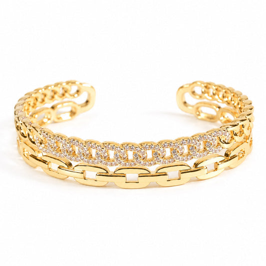 A gold chain link cuff bracelet featuring a central row of clear pavé stones, photographed on a clean white background.