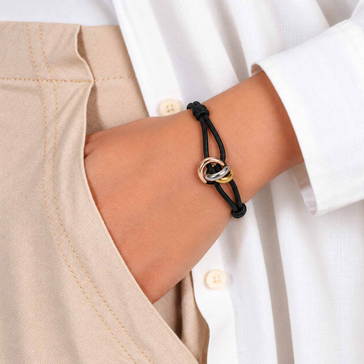 Black adjustable cord bracelet with intertwined rose gold, silver, and gold rings, styled on the wrist.