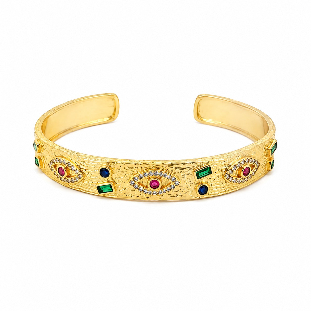 Anti-tarnish textured gold open cuff bracelet featuring evil eye motifs with pavé crystal borders and ruby-red centers, interspersed with bezel-set green emerald baguettes and deep blue sapphire round stones.