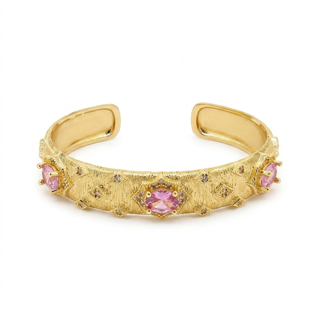 Anti-tarnish textured gold cuff bracelet featuring oval-cut pink gemstone centerpieces set in starburst frames with surrounding diamond-shaped pavé cz crystal accents and a brushed-matte finish.