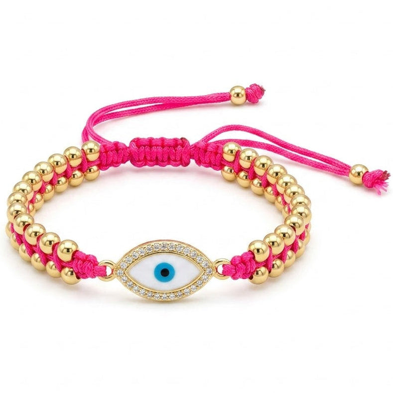 Hot pink braided cord bracelet with polished gold beads and a central oval blue evil eye charm. The charm is outlined with sparkling clear crystals and paired with adjustable pink cord ends. Displayed on a clean white background.