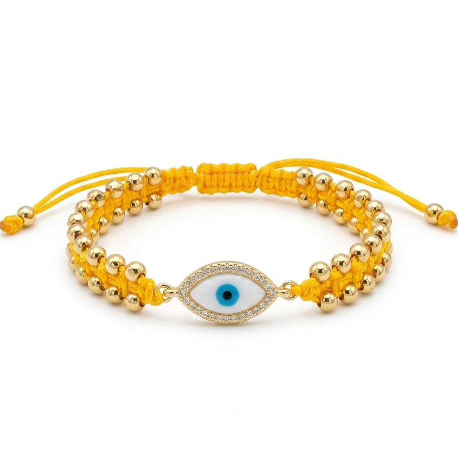 Yellow braided cord bracelet with polished gold beads and a central oval evil eye charm featuring a blue iris and black pupil. The charm is bordered with sparkling clear crystals and paired with adjustable yellow cord ends. Displayed on a clean white background.