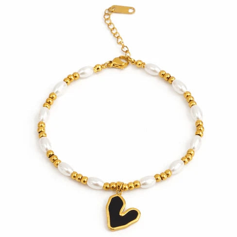 Gold-tone adjustable pearl bracelet featuring alternating white pearl-like beads and small gold beads, finished with a black enamel heart-shaped dangling charm.