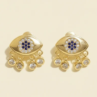 Gold-tone evil eye stud earrings featuring blue-and-white eye motifs surrounded by clear crystals, with multiple dangling crystal charms along the bottom edge.