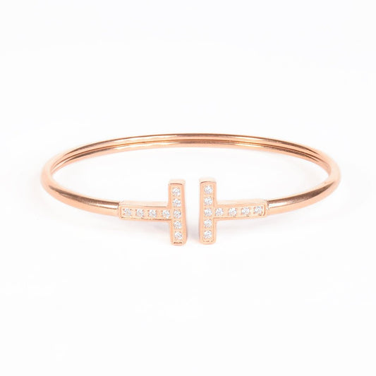 Linear cuff bangle with dual T motifs and sparkling crystal accents, finished with an anti-tarnish rose gold coating, perfect for everyday wear, modern styling, and elegant layering.
