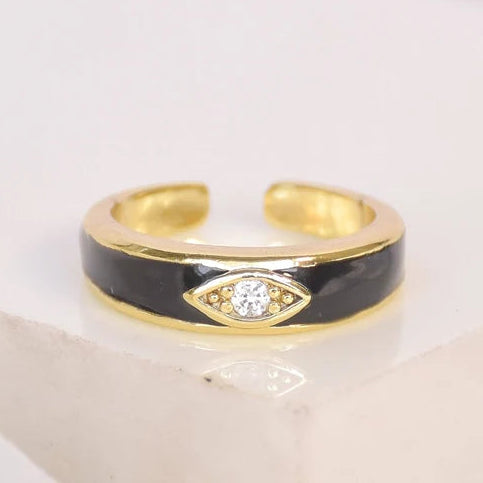 Gold and black open ring featuring an eye-shaped centerpiece with a sparkling crystal, photographed on a clean white background.
