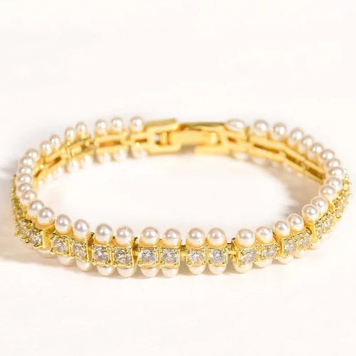 The image shows a gold-toned bracelet featuring a continuous border of small white pearls along the top and bottom, with a central row of square-cut clear stones set in gold. It has a polished gold clasp and is photographed in a clean white studio setting with bright lighting and soft shadows.