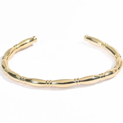The image shows a polished gold open cuff bangle with a smooth tubular design and several small decorative ringed bands placed along the bracelet. It has rounded open ends and is photographed on a clean white background with bright studio lighting and a soft natural shadow.