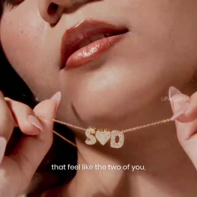 A short promotional jewelry video showcasing close-ups of a woman wearing various custom crystal-paved initial and heart charm necklaces against a white button-down shirt.