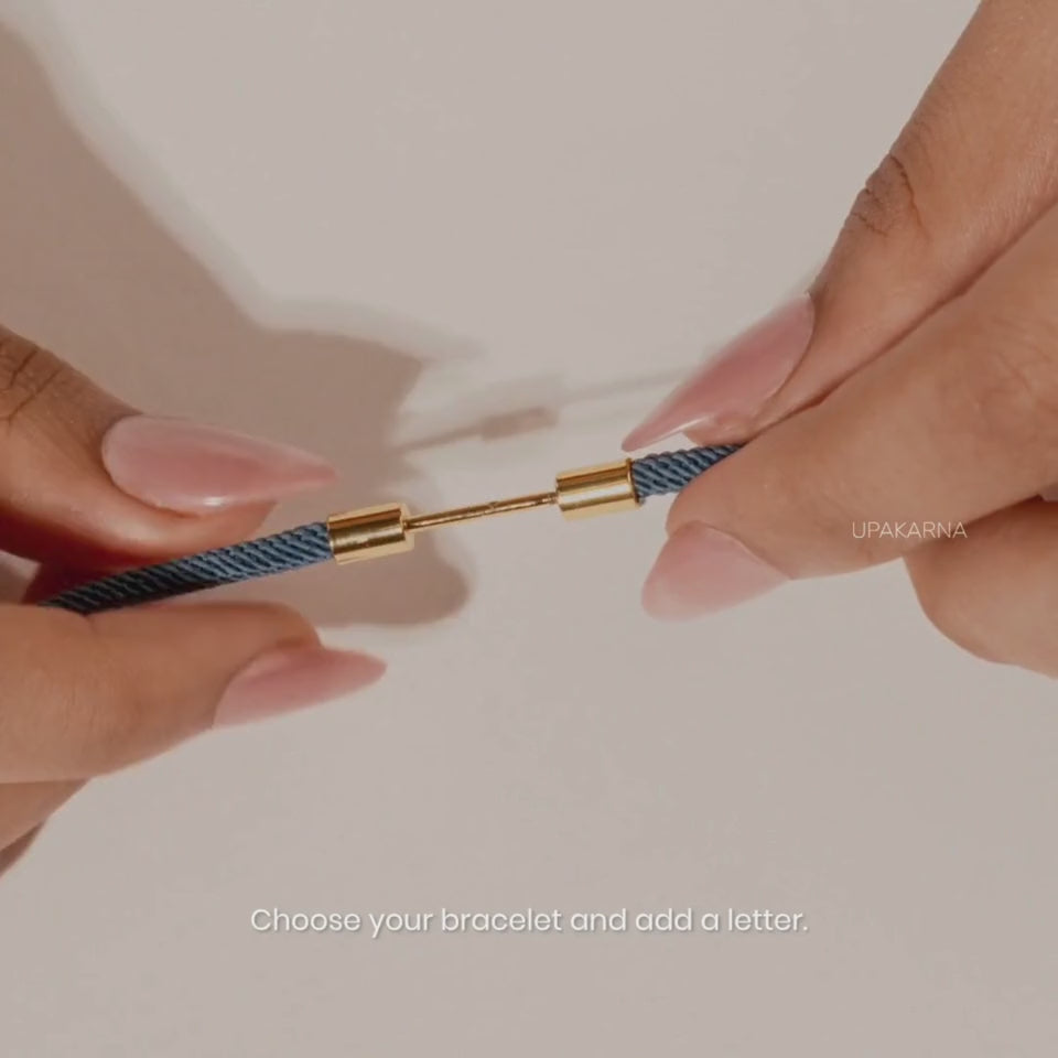 Video showing a navy blue cord bracelet being assembled with a gold-tone letter charm, highlighting its water-resistant design before showing the personalized bracelet worn on the wrist.