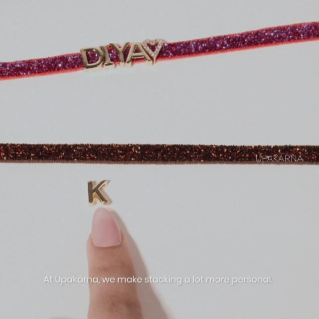 Video showcasing personalized Upakarna bracelets, with gold-tone initial charms and evil eye details being added to glittery bands and layered together into a personalized bracelet stack.