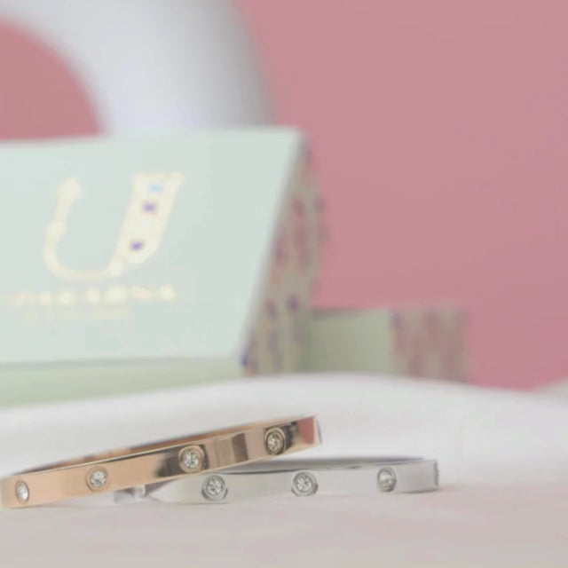 Elegant stainless steel bangle with a sleek push-lock design and polished finish, available in gold, rose gold, and silver, perfect for everyday wear, effortless stacking, and styling with watches.